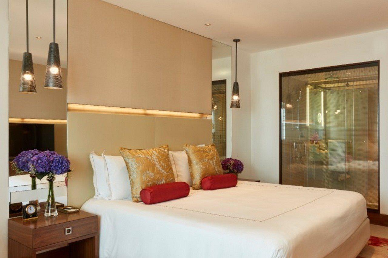 فندق ذا تاج محل تاور مومباي المظهر الخارجي الصورة The photo shows a modern bedroom with a stylish design. It features a large bed with white linens and decorative pillows in gold and red. The walls are neutral, and there are pendant lights hanging above the bed. To the side, there is a wooden nights
