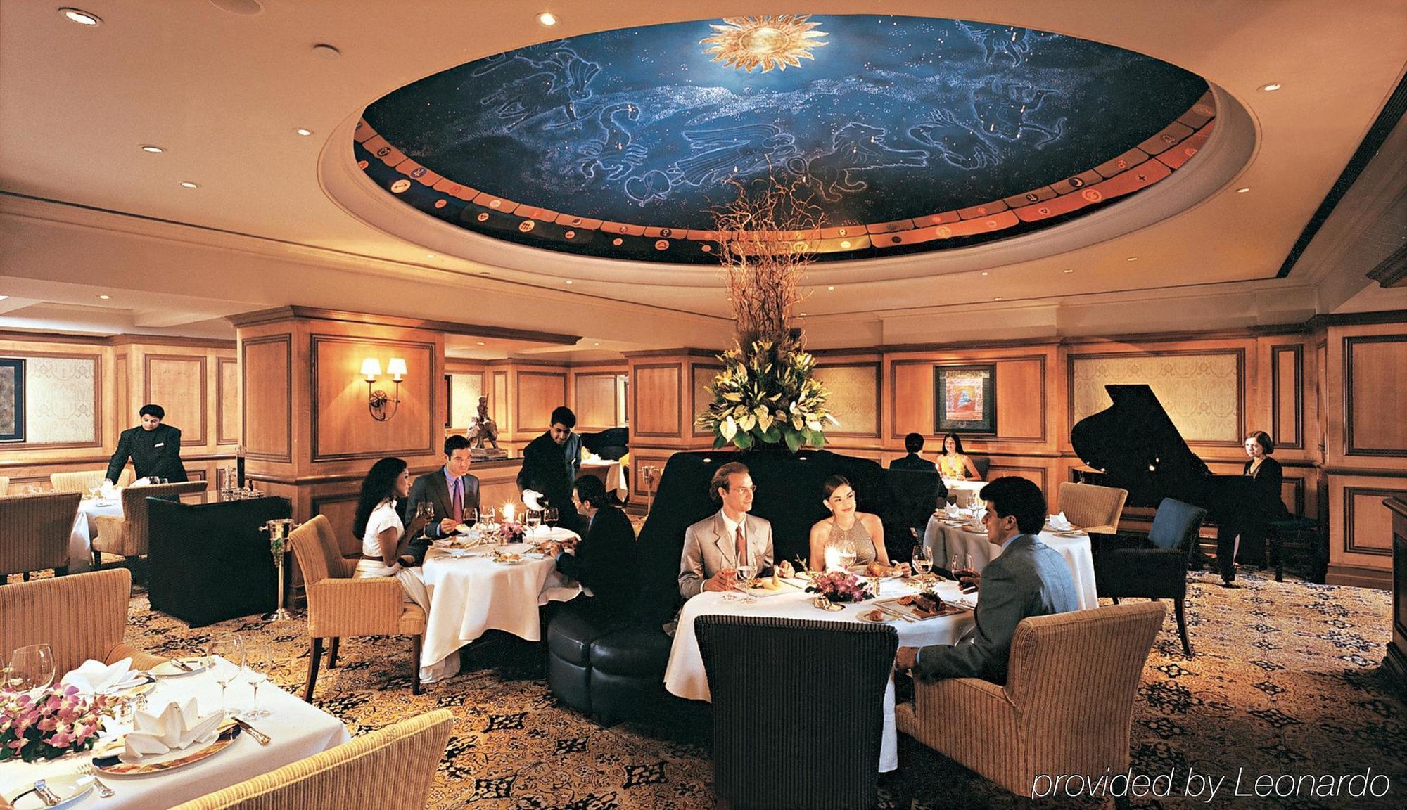 فندق ذا تاج محل تاور مومباي المظهر الخارجي الصورة The photo depicts an elegant dining room setting. The ceiling features a beautiful mural of the night sky, complete with stars and a shining sun. There are several tables set for dining, each with white tablecloths, flowers, and fine dining arrangeme