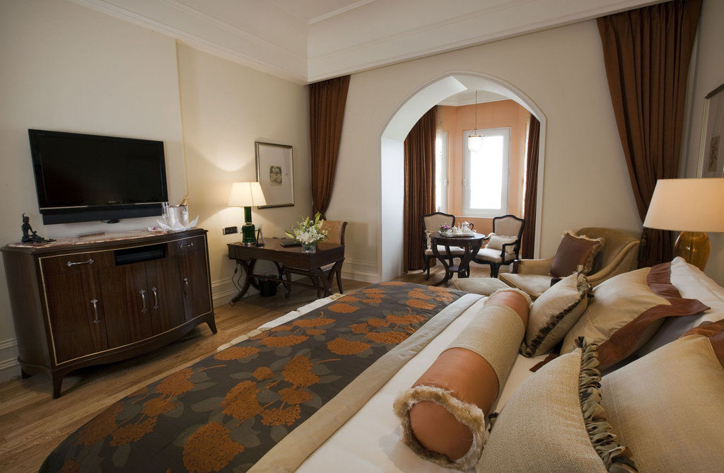 فندق ذا تاج محل تاور مومباي المظهر الخارجي الصورة The photo shows a beautifully arranged hotel room featuring a king-size bed with decorative pillows and a stylish bedspread. Beside the bed is a modern wooden dresser with a flat-screen TV mounted on the wall. There is a cozy seating area with two ch